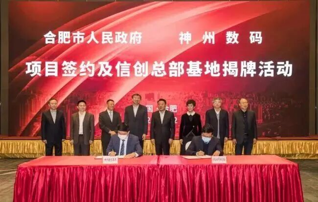 图片展示了合肥市人民政府与神州数码项目签约及信创总部基地揭牌活动。背景为红色，上方有“合肥市人民政府 神州数码”字样，下方是“项目签约及信创总部基地揭牌活动”标题。画面中有两位男士在桌前签字，桌前有红色桌布，背景还有多人站立。该图片与上下文紧密相关，直观呈现了合肥在产业培育过程中与企业合作、推动项目落地的场景，体现了合肥在资本招商方面的努力。