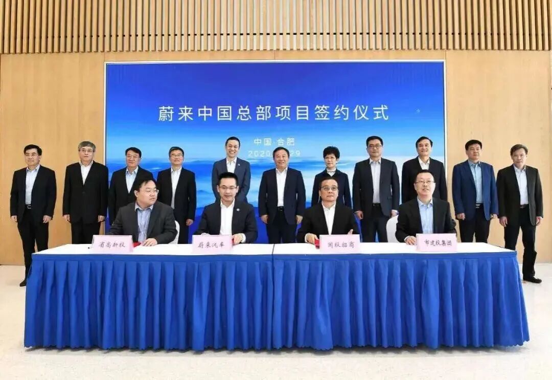 图片为蔚来中国总部项目签约仪式现场。背景板上写着“蔚来中国总部项目签约仪式 中国·合肥 2020年7月29日”。台前有八位男士，其中四位坐在台前，分别代表蔚来中国、蔚来汽车、蔚来中国合肥公司、合肥市政府。背景板上方有蓝色渐变的海景图案。该图片与上文提到的2019年合肥拿出70亿元“招安”巨亏百亿的蔚来汽车落户发展新能源汽车，以及蔚来将总部正式落户合肥的内容相呼应，直观呈现了签约仪式场景。